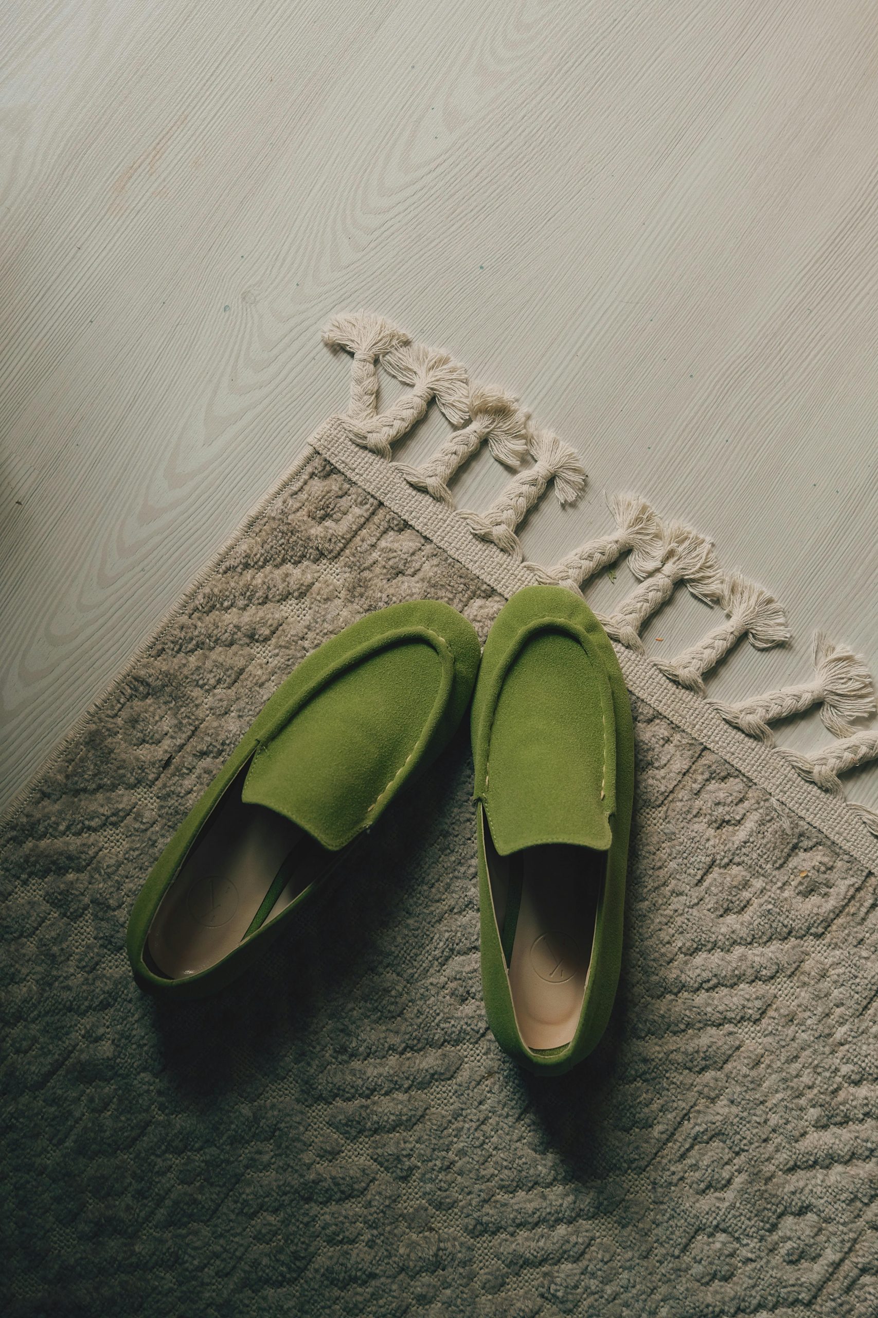 Top view of elegant green moccasins on a textured beige rug indoors.